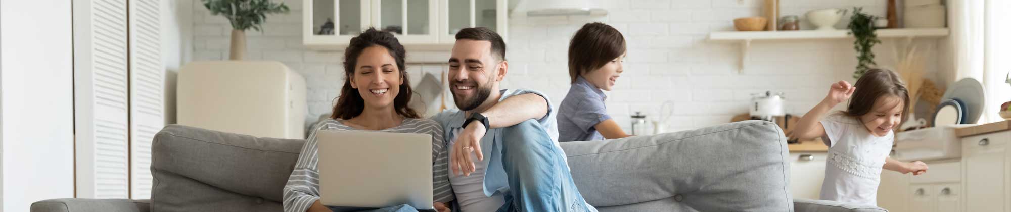 daughter and son running around parents siting on sofa using laptop